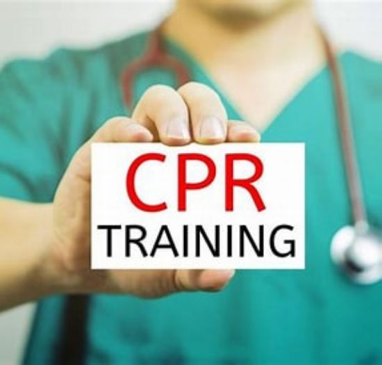 A healthcare professional in green scrubs holds a white card with bold red and black text that reads "CPR Training."